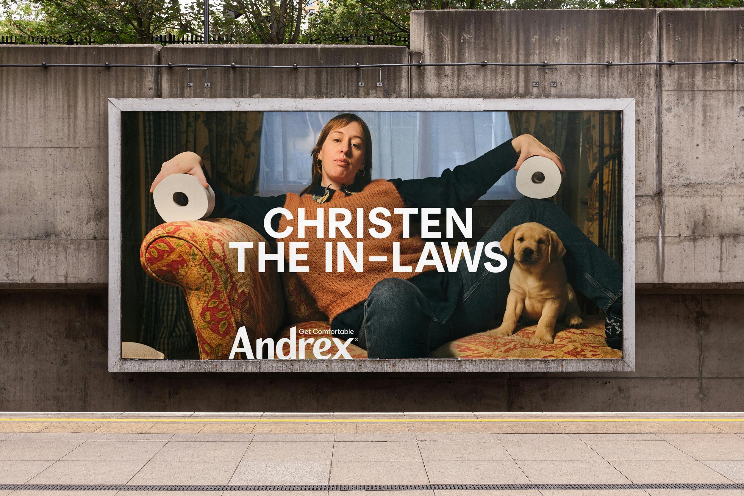 A billboard advertisement featuring a woman and a dog promoting Andrex toilet paper with the caption "Christen The In-Laws"